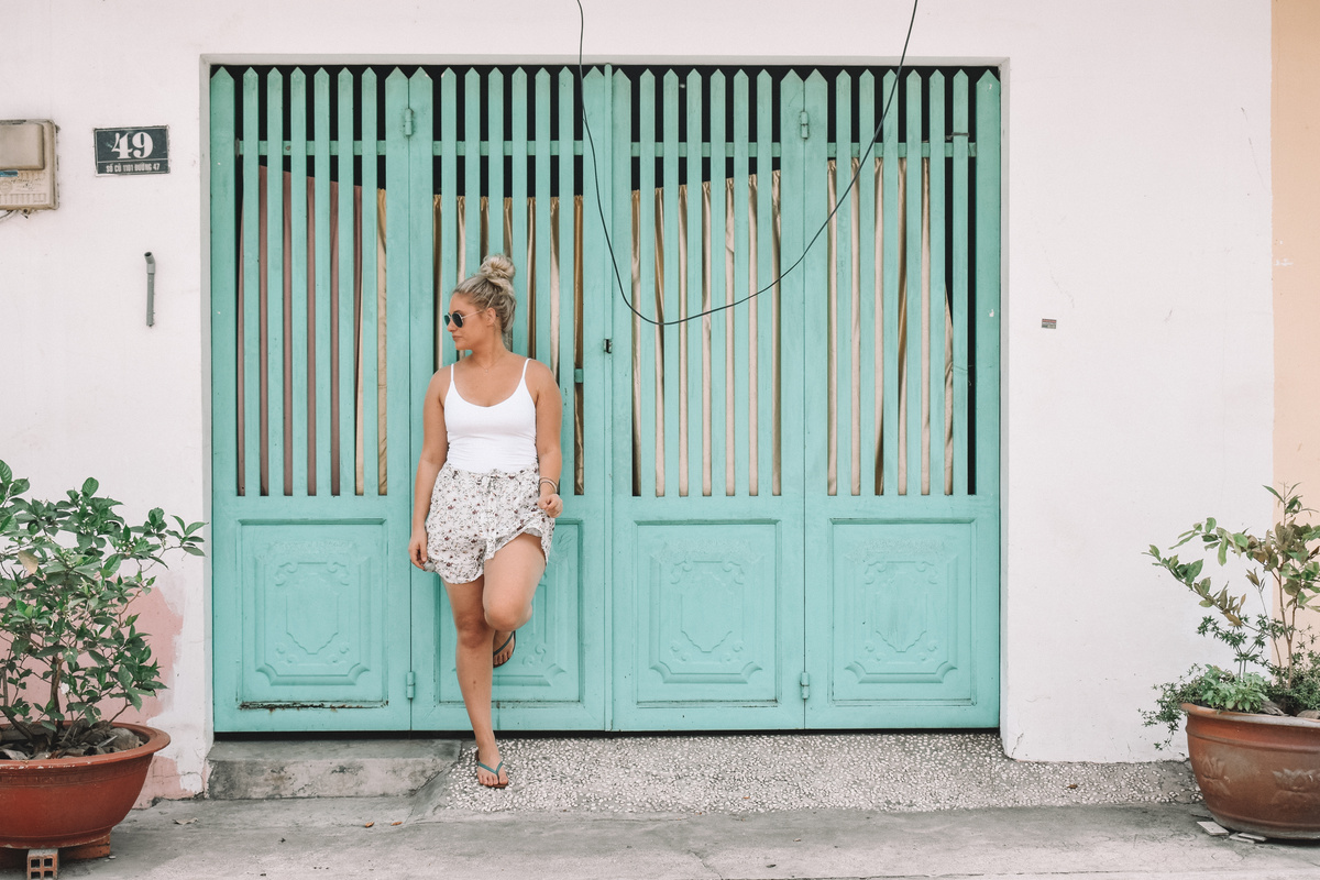 Woman in White Tank Top Leaning on Teal Gate